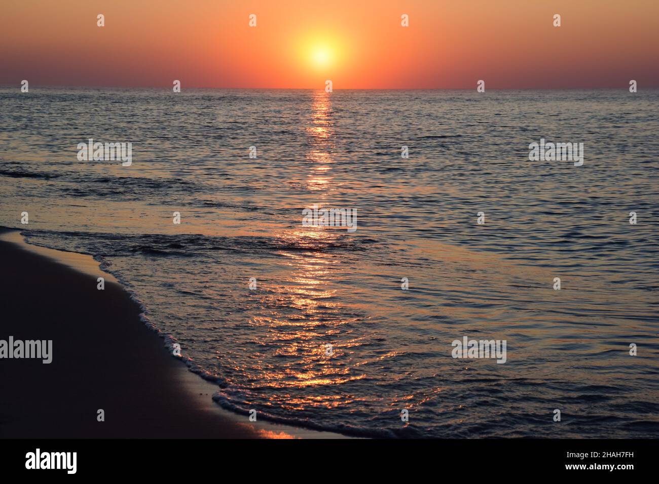 Morgendämmerung Sonne vor dem Hintergrund des Meeres Sandstrand, mit Reflexionen auf den ruhigen Wellen Stockfoto