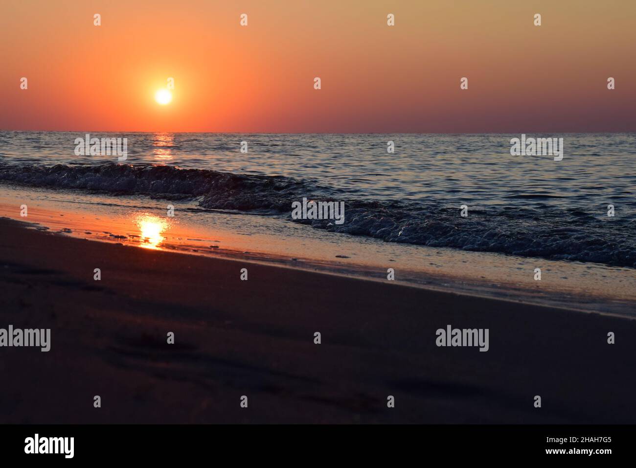 Morgendämmerung Sonne vor dem Hintergrund des Meeres Sandstrand, mit Reflexionen auf den ruhigen Wellen Stockfoto