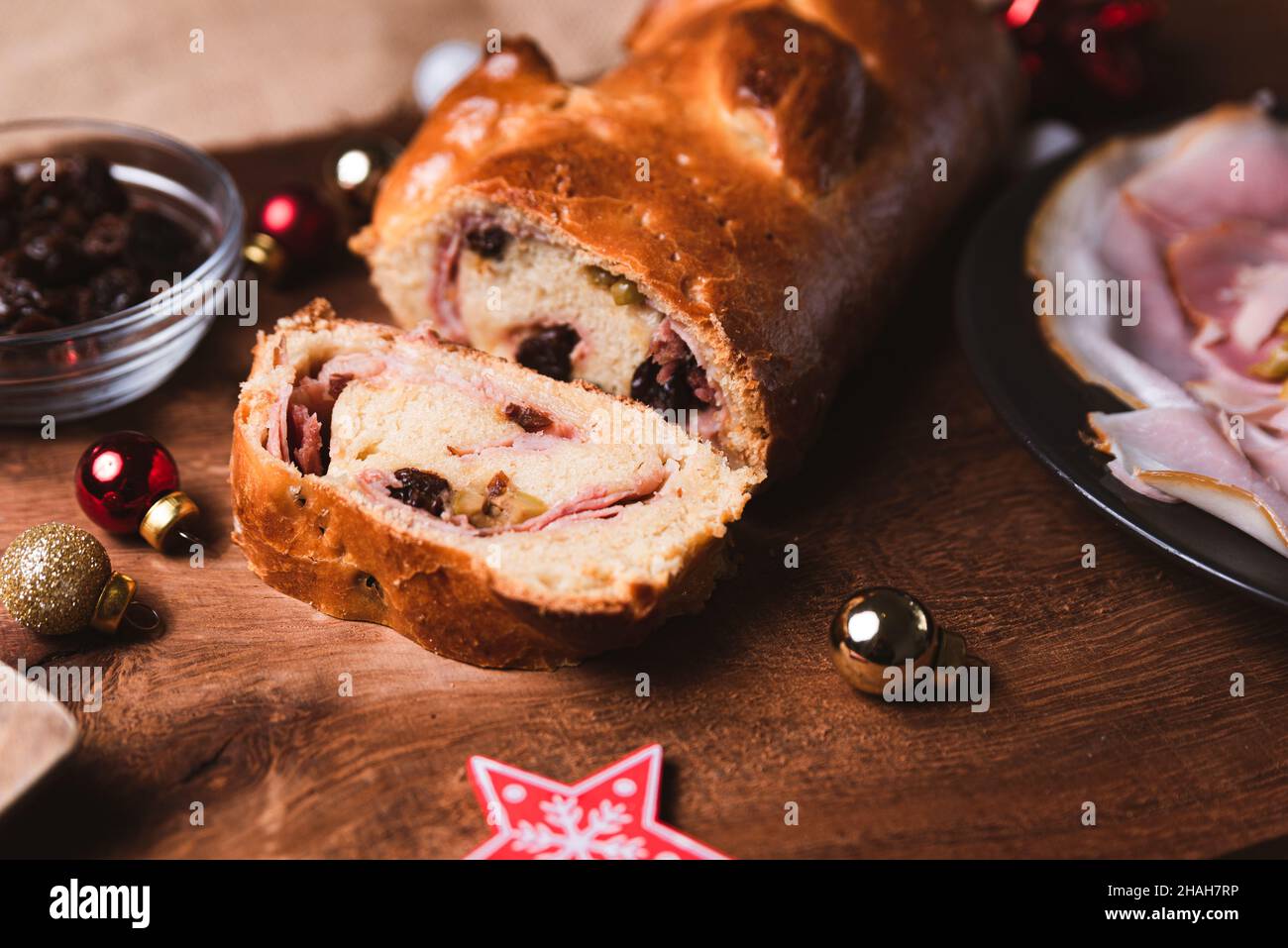 Traditionelles venezolanisches Gericht, bekannt als „Pan de jamon“, was Schinken mit Brot und Weihnachtsschmuck auf einem Holztisch bedeutet, mit Schinken, Oliven, Rosinen und mir Stockfoto