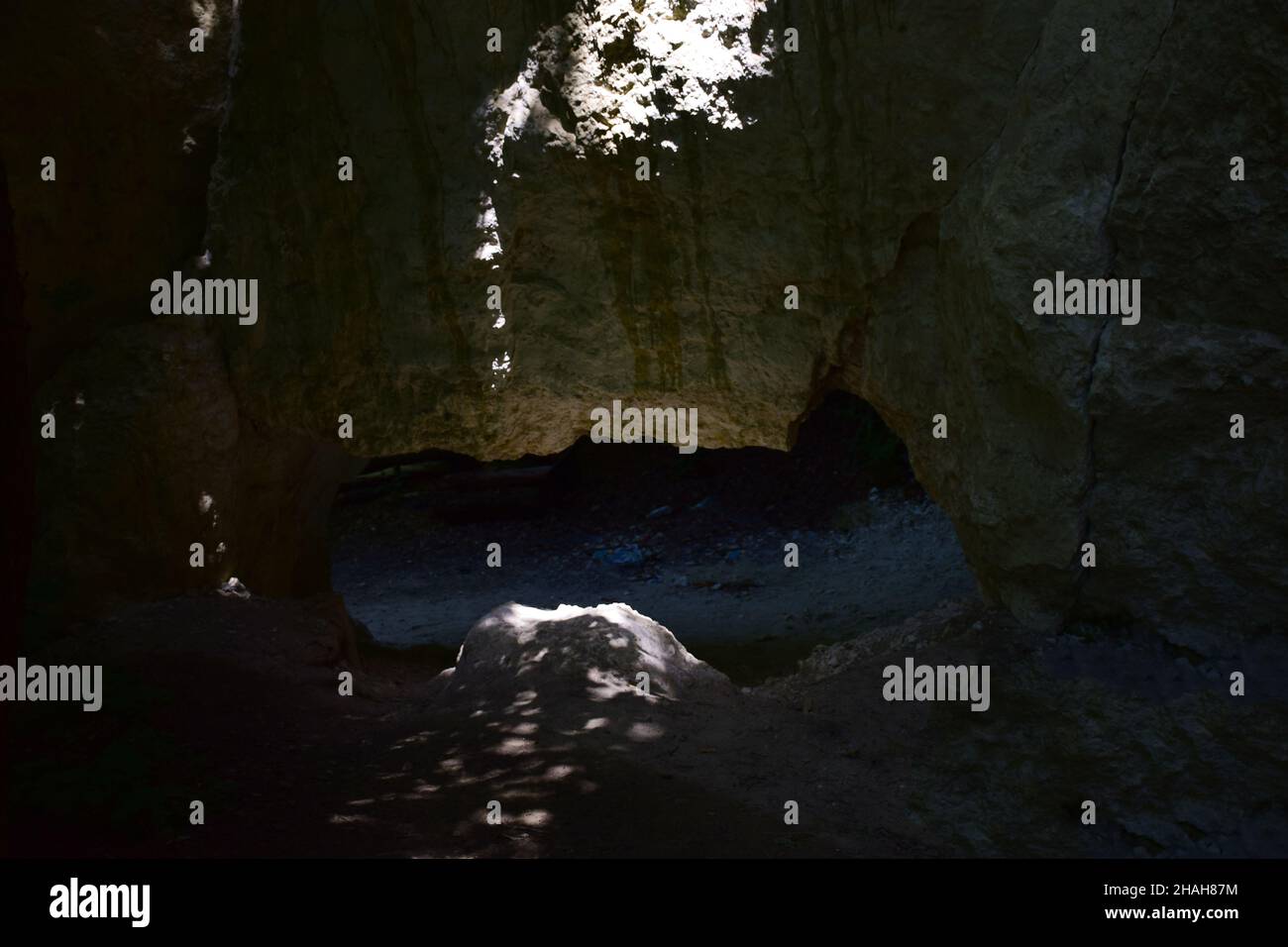 Enger Eingang zu einer unterirdischen Höhle oder Grotte, die nur leicht durch Sonnenlicht beleuchtet ist Stockfoto