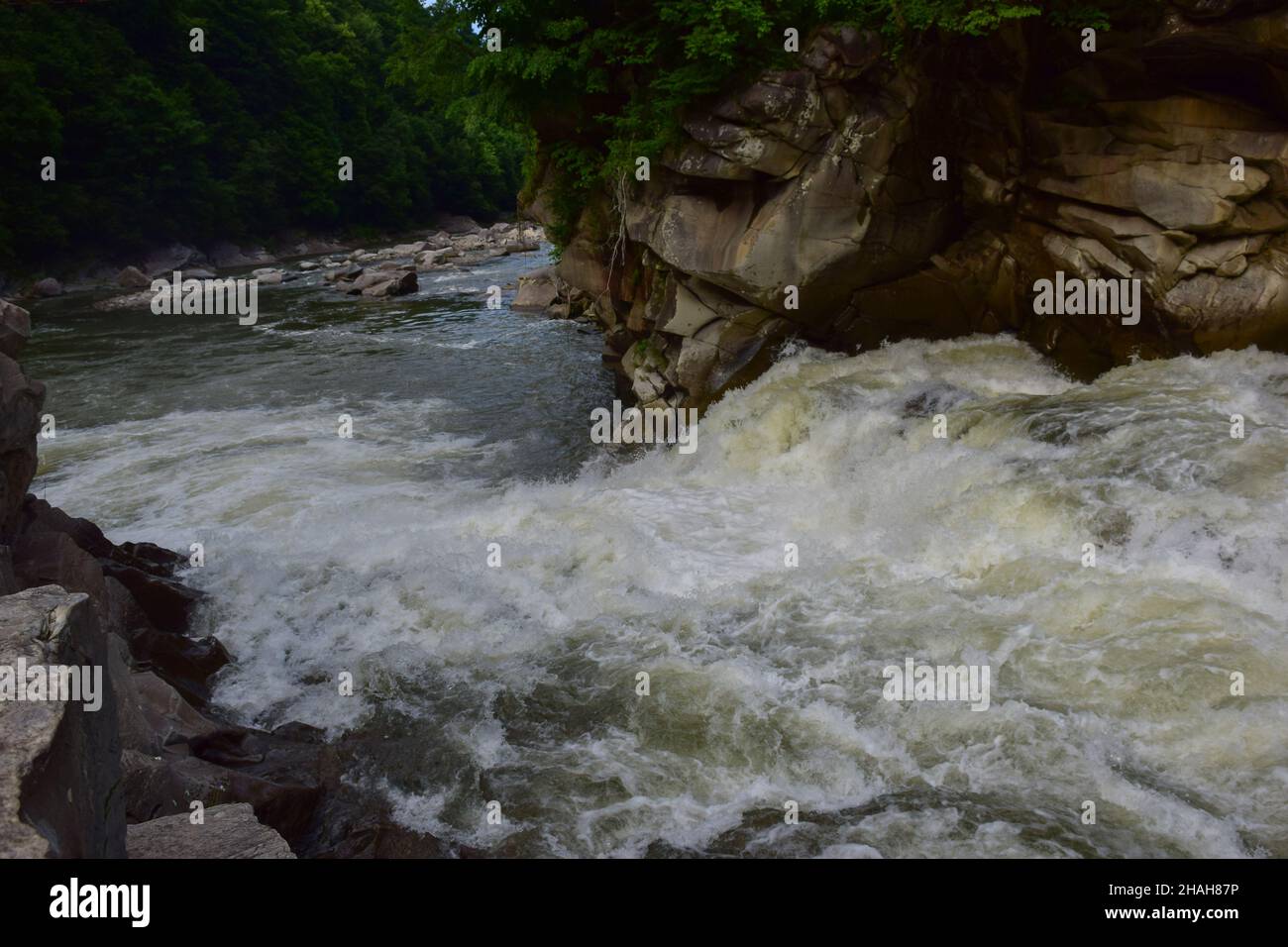 Zwischen den felsigen Ufern fließt ein stürmischer Gebirgsfluss mit einem schäumenden Wasserfall Stockfoto