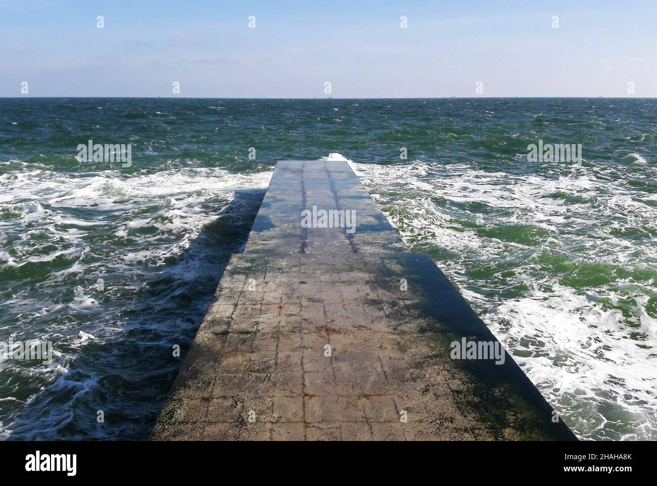 Ein steinerner Wellenbrecher, der sich bis weit in das kalte Wintermeer mit schäumenden Wellen in die Perspektive ausdehnt. Es gibt niemanden auf dem Pier. Stockfoto