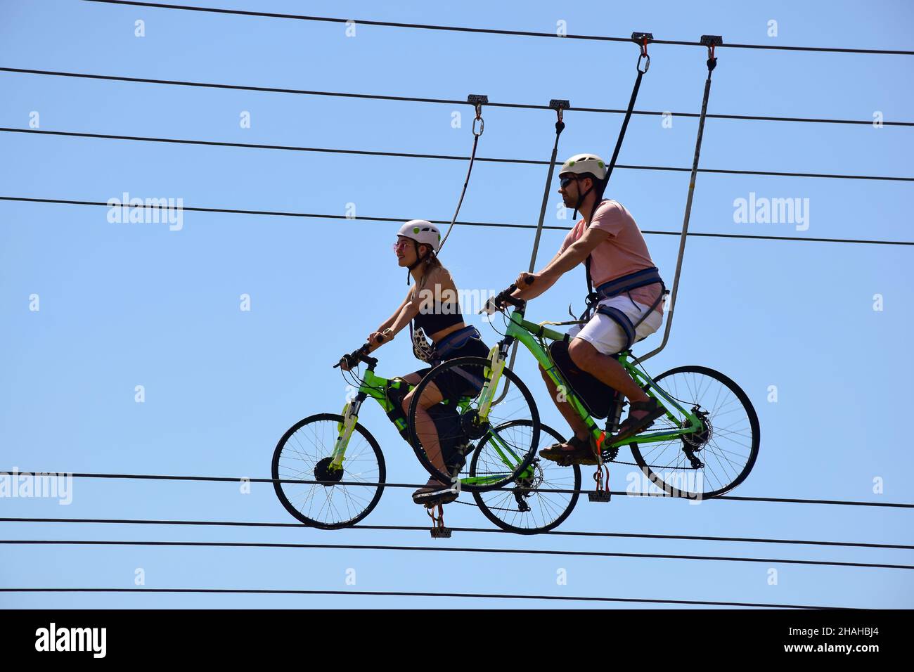 Bei der Attraktion fahren ein Mann und ein Mädchen auf Fahrrädern an Hängeseilen und lächeln. Von unten gegen den blauen Himmel fotografiert Stockfoto