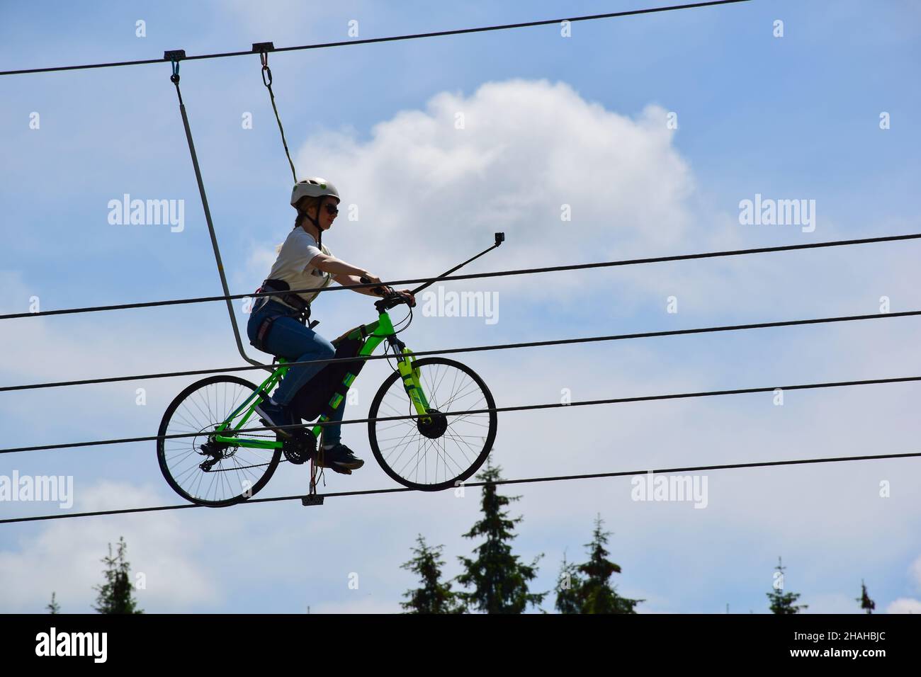 Das Mädchen fährt auf einem Drahtseil mit dem Fahrrad, trägt einen Helm und eine Sonnenbrille und macht ein Selfie. Attraktion auf einem Hintergrund von blauem Himmel Stockfoto