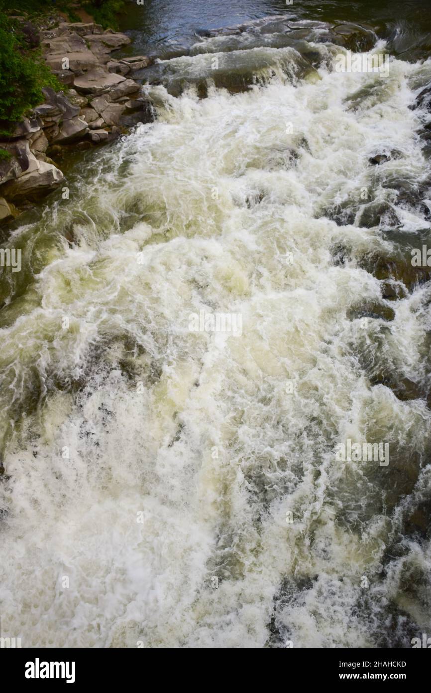 Zwischen den felsigen Ufern fließt ein stürmischer Gebirgsfluss mit einem schäumenden Wasserfall Stockfoto