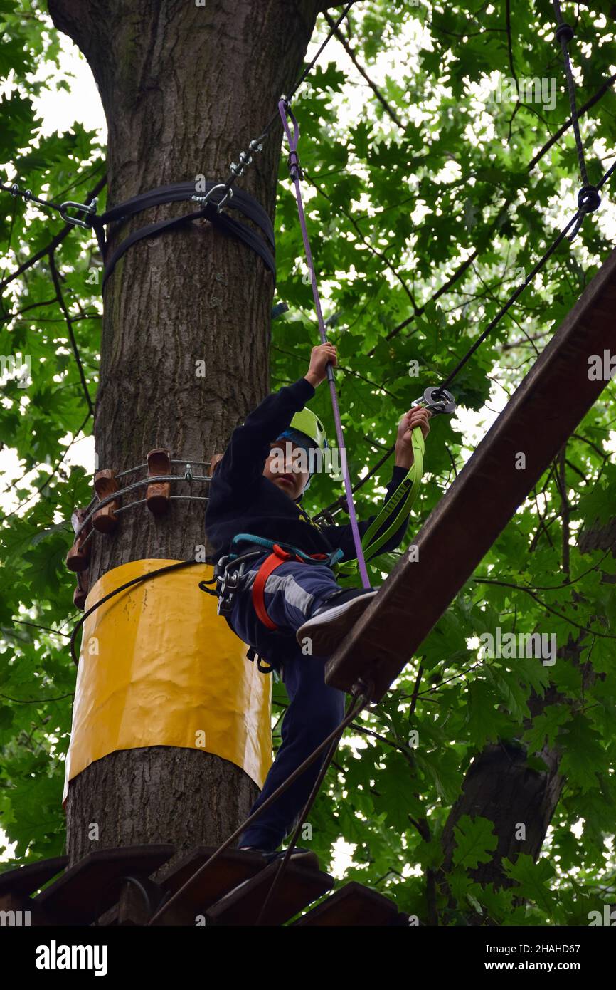 Ein Teenager in einem Schutzhelm klettert in einem Seilpark auf eine Hängeleiter Stockfoto