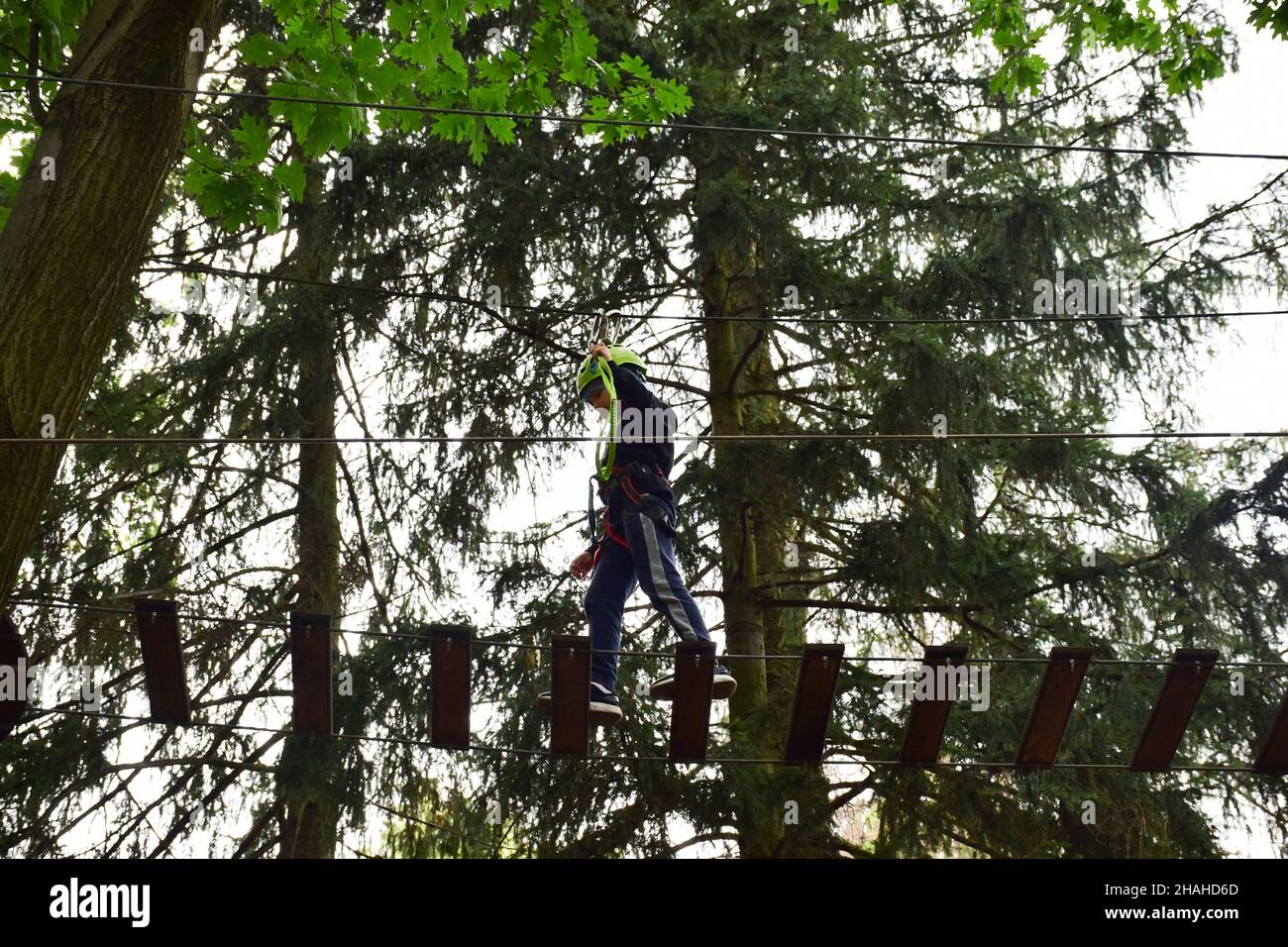 Ein Teenager in einem Schutzhelm klettert in einem Seilpark auf eine Hängeleiter Stockfoto