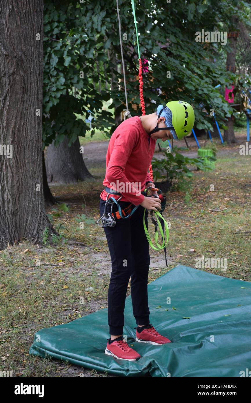 Ein Teenager Junge in Sportausrüstung zum Klettern von Bäumen und Felsen trennt den Karabiner von der Ausrüstung Stockfoto