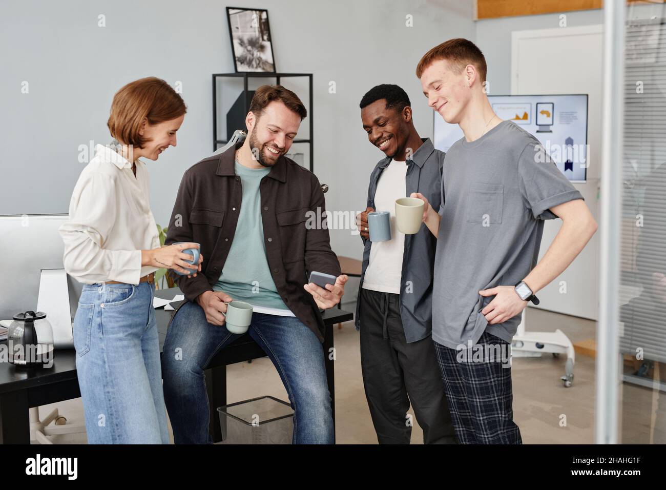 Ein junger Geschäftsmann zeigt seinen Kollegen etwas auf dem Handy, während sie im Büro Kaffee trinken Stockfoto