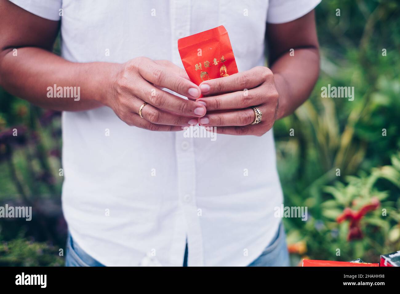 Die Hände eines Mannes, der einen geöffneten roten Umschlag oder ein rotes Paket mit den Namen Ang Pao oder Ang Pow hält, auch Hongbao oder Hungbao in Mandarin und Lai See in Kantonesisch. Stockfoto