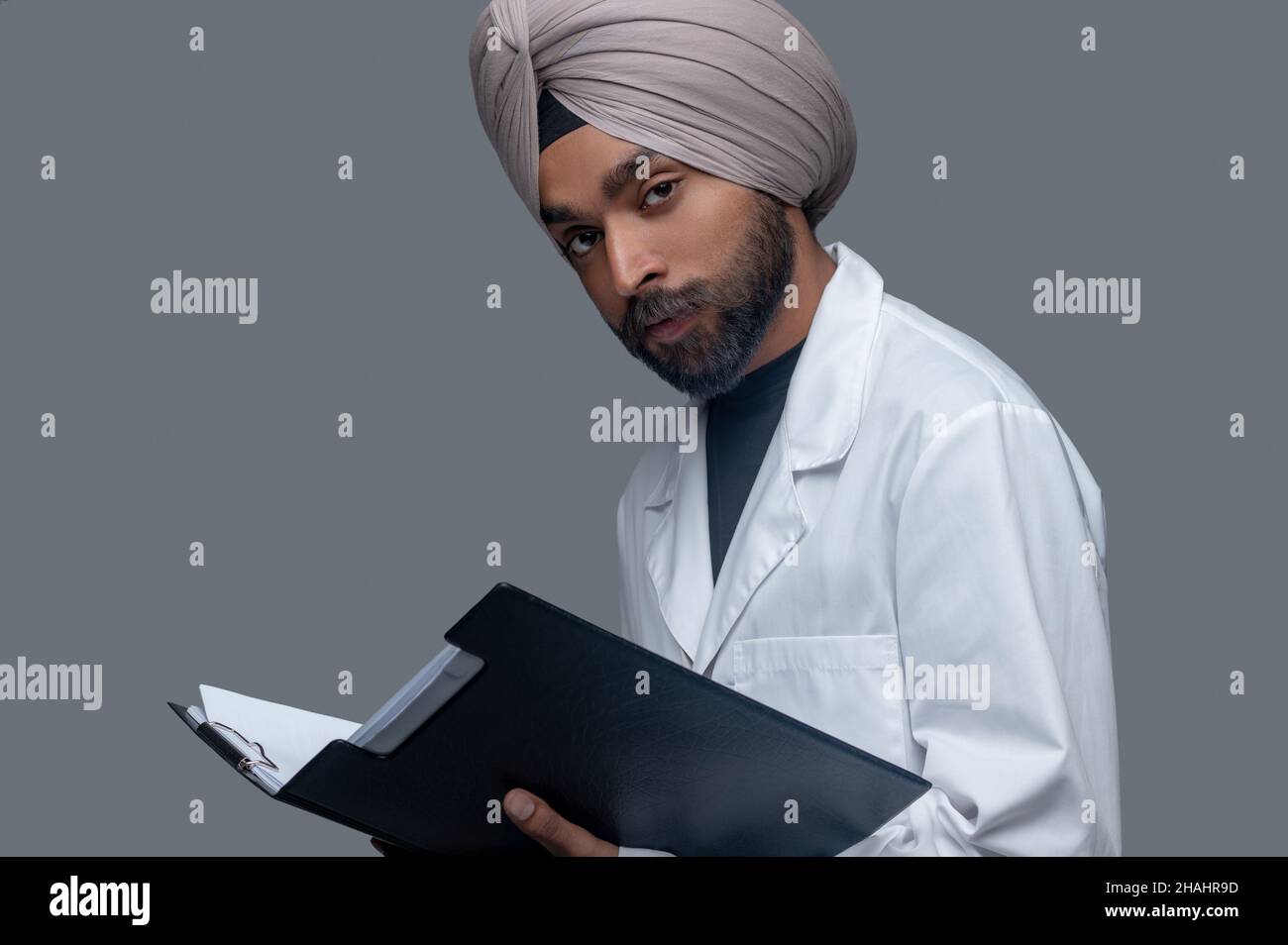 Ruhiger indischer Arzt im Turban, der medizinische Dokumente hält Stockfoto