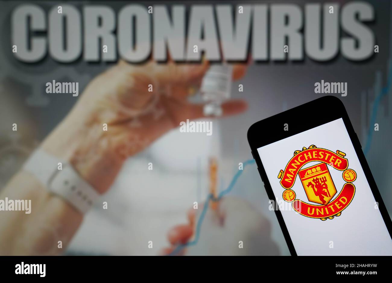 Aktenfoto vom 09-01-2021 des Manchester United Football Club-Logos, das auf einem Mobiltelefon mit einer Coronavirus-Abbildung auf einem Monitor im Hintergrund angezeigt wird. Manchester United führt Gespräche mit der Premier League darüber, ob das morgige Spiel in Brentford Schieß los. sollte, und hat den Betrieb der ersten Mannschaft auf ihrer Trainingsbasis in Carrington für 24 Stunden eingestellt, um das Risiko weiterer Covid-19-Infektionen zu minimieren, teilte der Club mit. Ausgabedatum: Montag, 13. Dezember 2021. Stockfoto