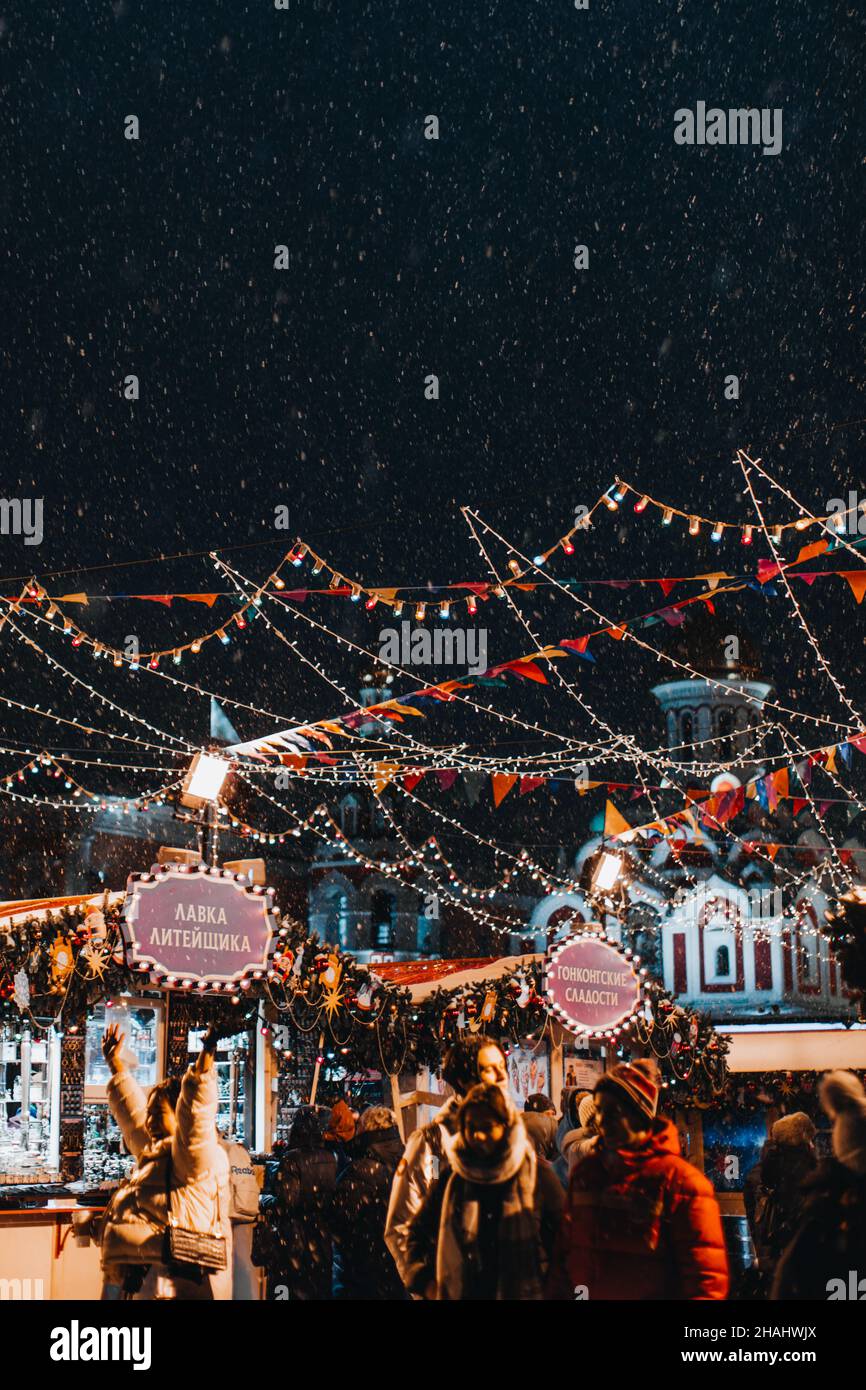 Hölzerner Weihnachtsstand auf dem Weihnachtsmarkt in der Abendzeit. Weihnachtsmarkt in Moskau mit hängenden Girlanden. Magische Winterzeit Stockfoto