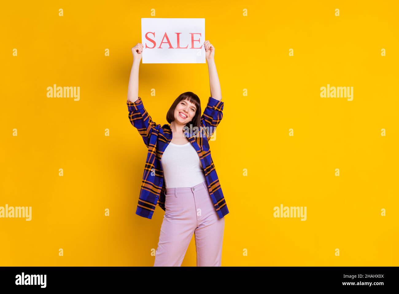 Portrait von attraktiven fröhlichen Mädchen hält in den Händen Verkauf Wort Poster Board neue Neuheit isoliert über helle gelbe Farbe Hintergrund Stockfoto