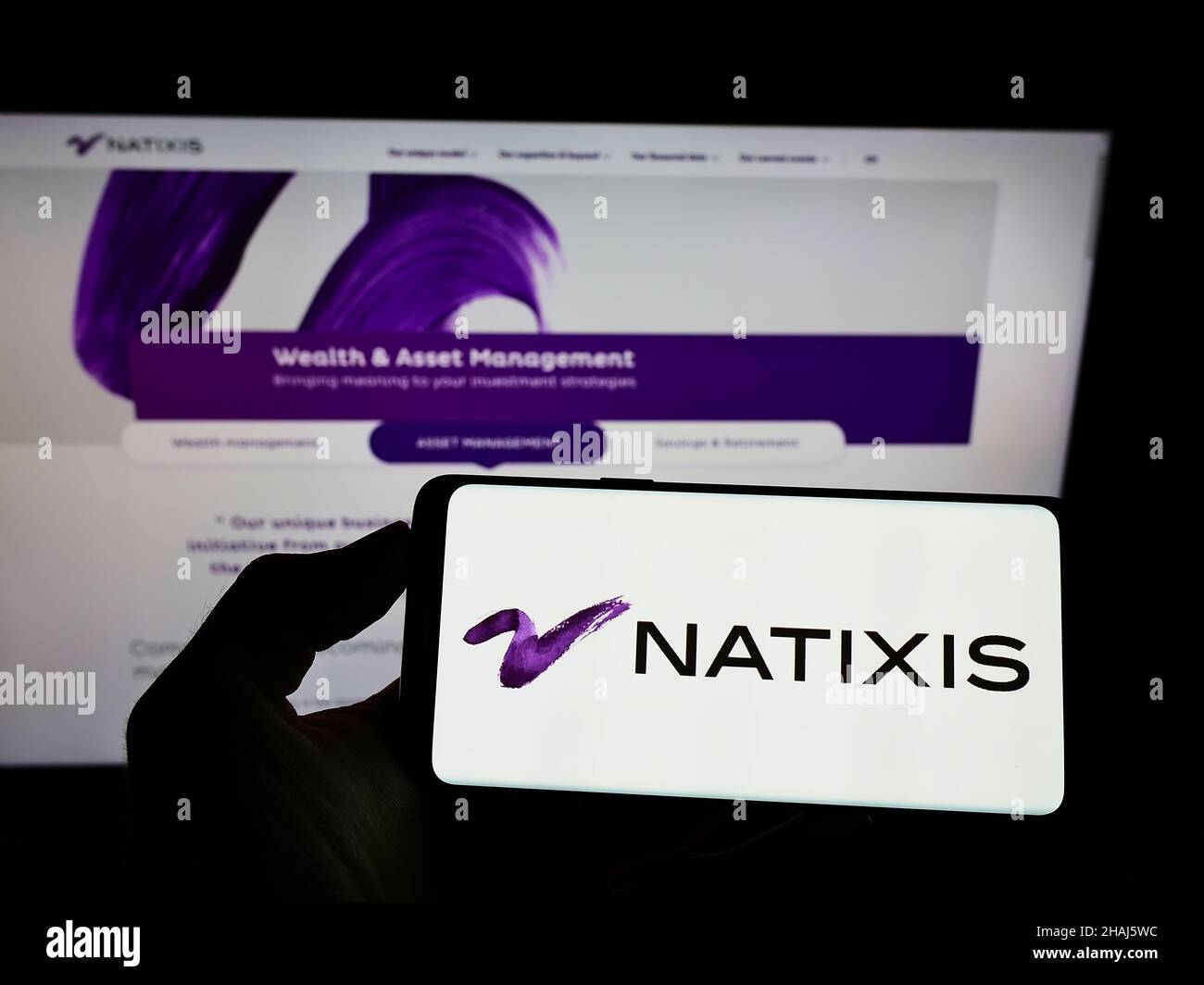 Person, die ein Mobiltelefon mit dem Logo der französischen Investmentgesellschaft Natixis S.A. auf dem Bildschirm vor der Business-Webseite hält. Konzentrieren Sie sich auf die Telefonanzeige. Stockfoto