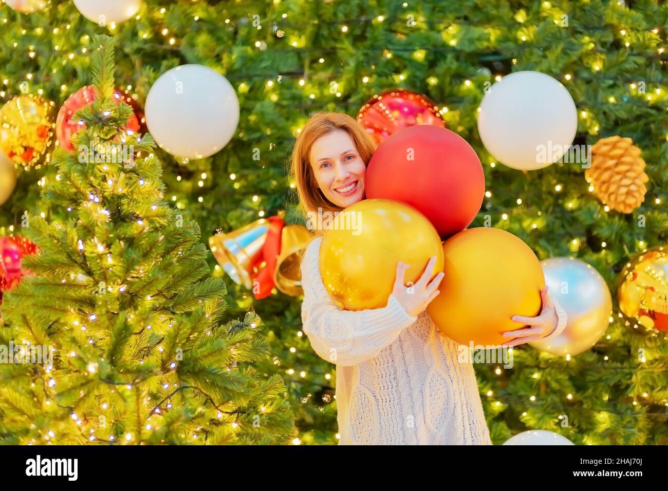 Fröhliches Mädchen hält große Weihnachtskugeln in der Nähe funkelnde Weihnachtsbäume. Festliche Atmosphäre. Stockfoto