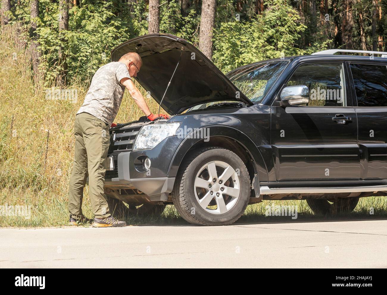 Fahrer steht und schaut in die Motorhaube mit Problem nach der Auto Pause im Sommer Reise. Stockfoto