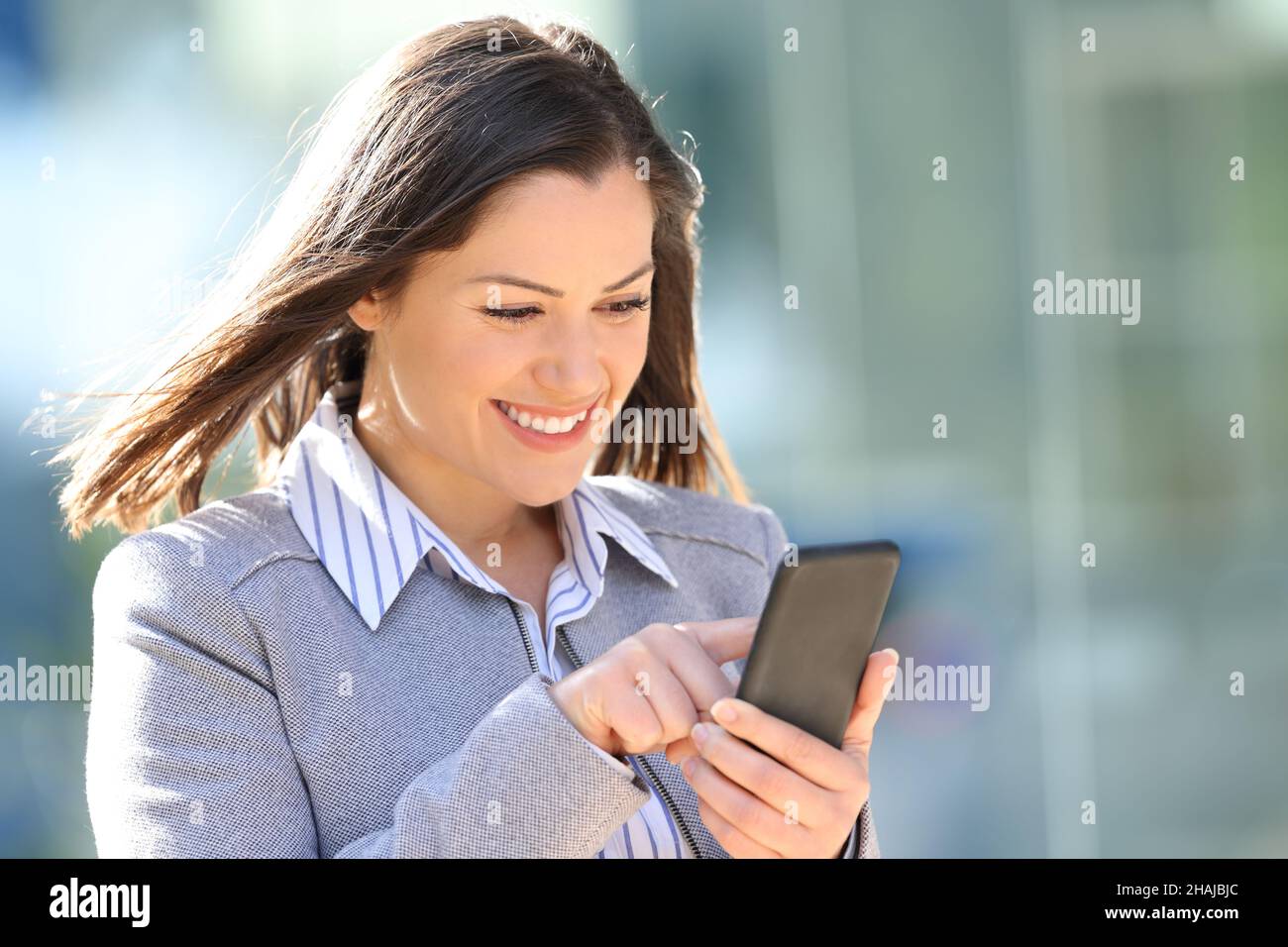 Eine glückliche Geschäftsfrau, die ihr Smartphone überprüft und auf der Straße ins Freie geht Stockfoto
