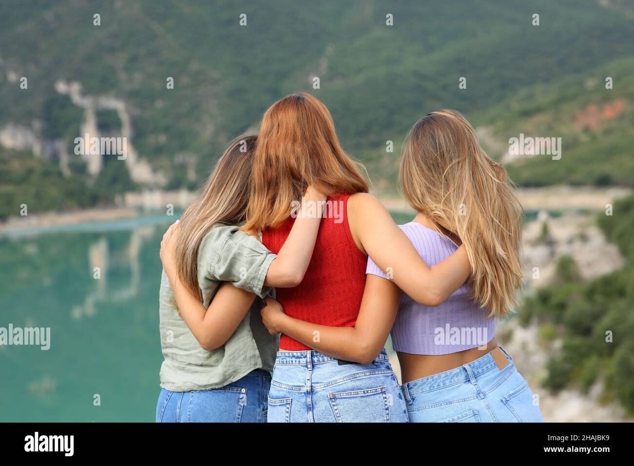 Rückansicht Porträt von drei Freunden, die während der Sommerferien den Blick auf einen See betrachten Stockfoto