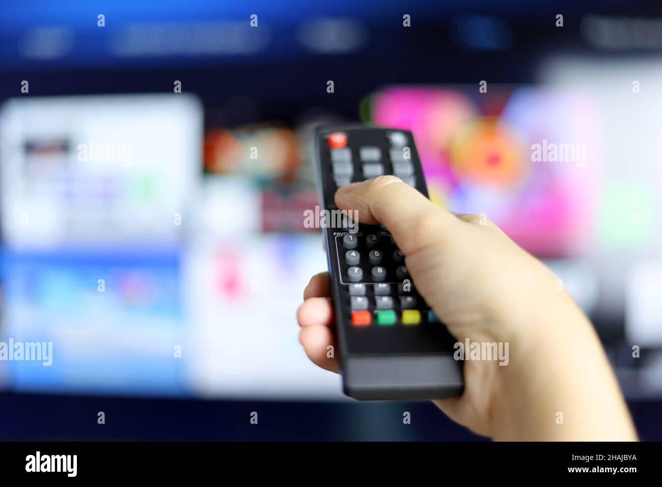 Weibliche Hand mit Fernbedienung auf Smart TV-Bildschirm Hintergrund. Frau, die Streaming-Dienste wählt, Filme ansieht Stockfoto