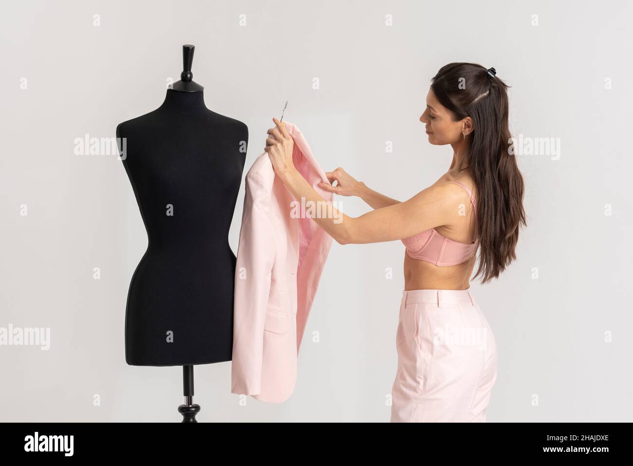 England, Großbritannien. 2021. Junge Frau, die nach dem Pressen eine rosa Jacke von einem Schneiderpummy entfernt hat. Stockfoto