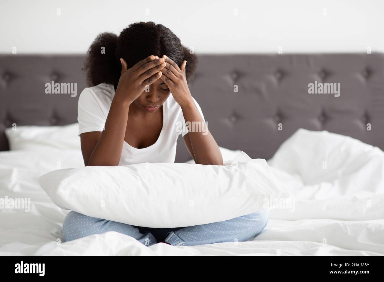 Verärgerte schwarze Frau, die im Bett saß und ihren Kopf berührte Stockfoto