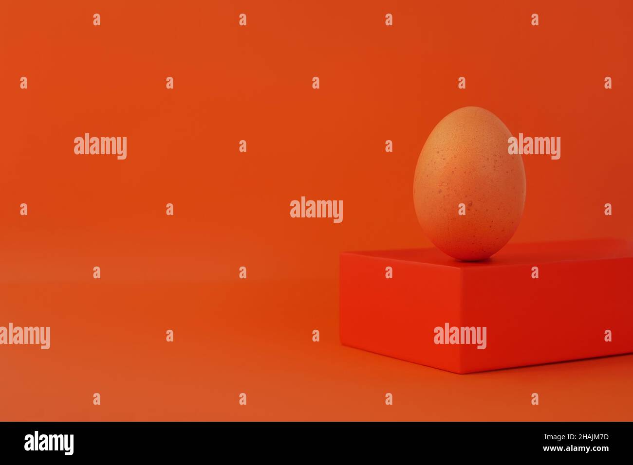 Osterei auf geometrische Form Podium Bühne orange Hintergrund Braun Huhn Ei balancieren Sockel isometrischen Minimalismus Stockfoto