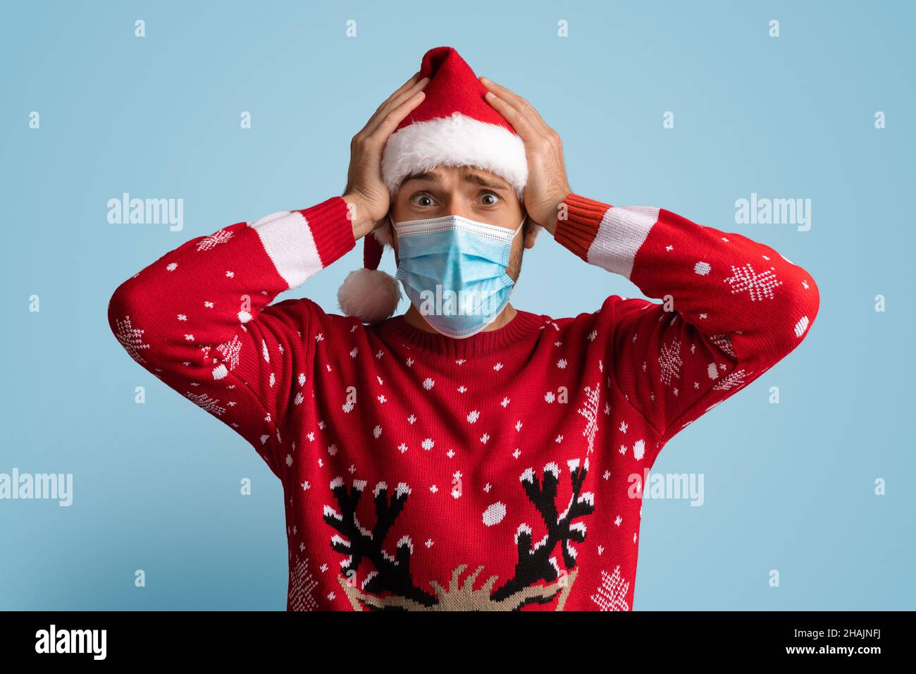 Weihnachtliche Sperre. Schockierter Junger Mann Mit Weihnachtsmütze Und Medizinischer Gesichtsmaske Stockfoto