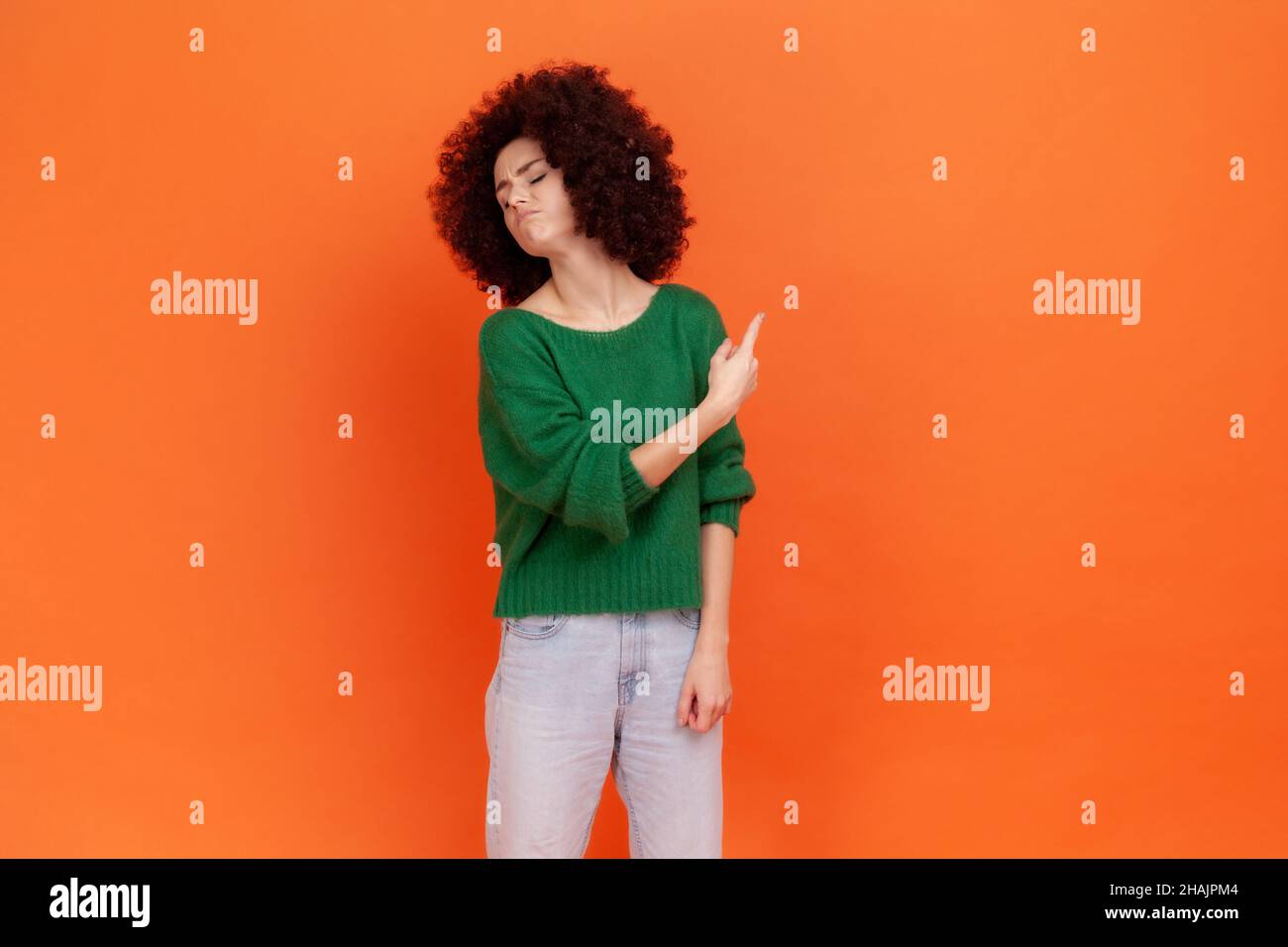 Raus. Frau mit Afro-Frisur trägt grünen lässigen Stil Pullover zeigt weg, schimpfen für schlechtes Ergebnis und zeigt Ausfahrt, Bestellung zu verlassen. Innenaufnahme des Studios isoliert auf orangefarbenem Hintergrund. Stockfoto