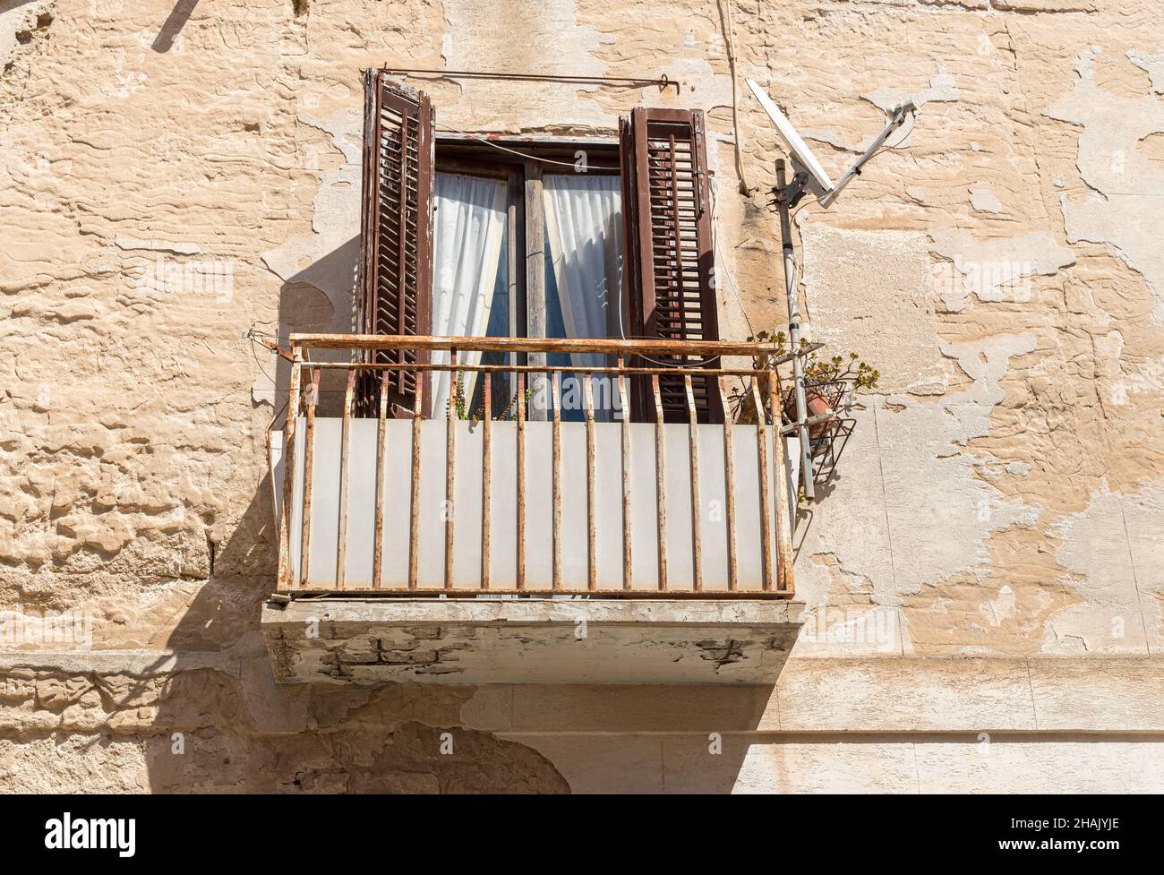 Alter Balkon mit alten hölzernen Fensterläden an der Steinmauer des typischen alten mediterranen Hauses in Sizilien. Stockfoto