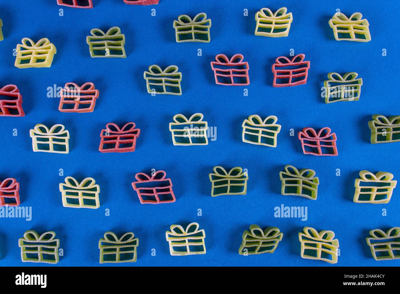 Kreativer Hintergrund für den Urlaub. Rohe Pasta in Form von Weihnachtsgeschenk in grünen, roten und gelben Farben auf blauem Hintergrund. Nahaufnahme. Flach liegend. Stockfoto