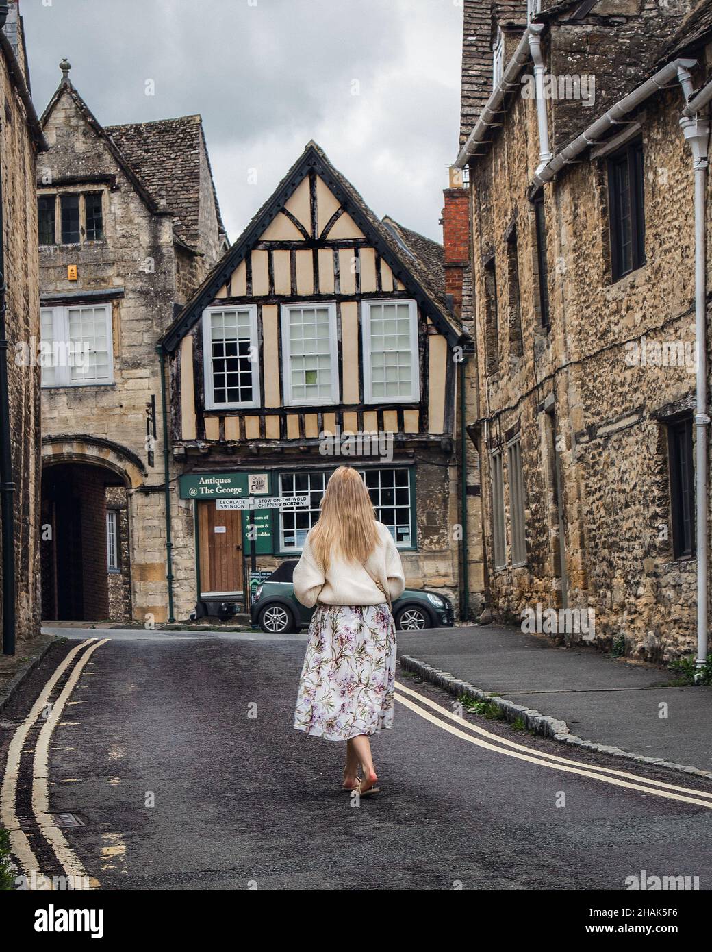 Frau, die eine Straße in Burford, einer Stadt am Fluss Windrush, in den Cotswold Hills, im West Oxfordshire District von Oxfordshire, England, entlang geht. Stockfoto
