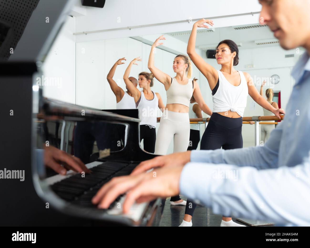 Ballettschüler machen Übungen in der Nähe von Barre mit Musiker am Klavier im Vordergrund Stockfoto