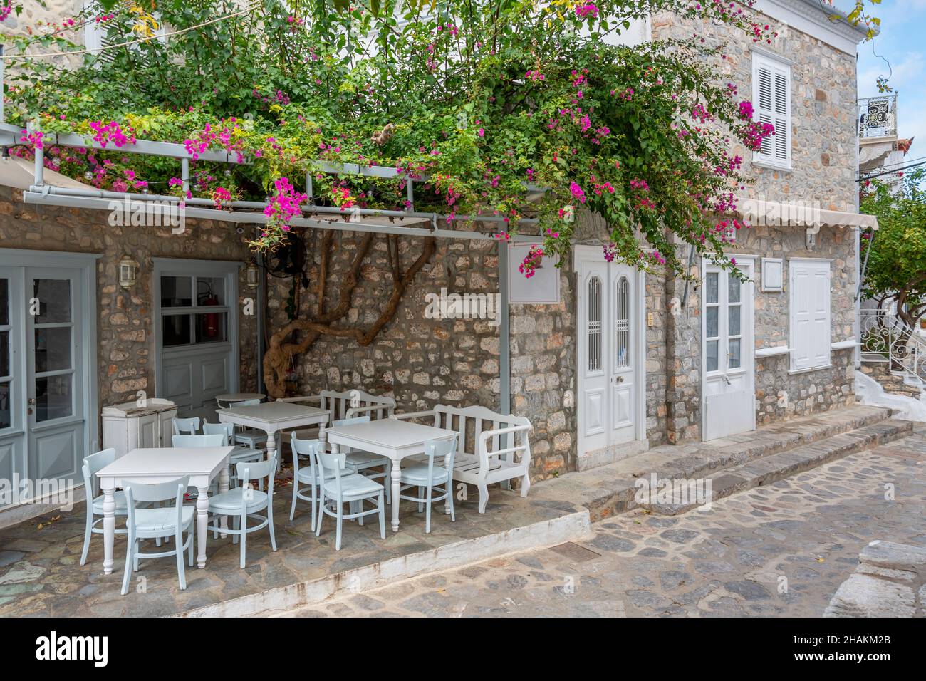 Eine malerische Straße mit weiß getünchten Häusern und einem kleinen Café im Freien im Dorf der kleinen griechischen Insel Hydra, Griechenland. Stockfoto