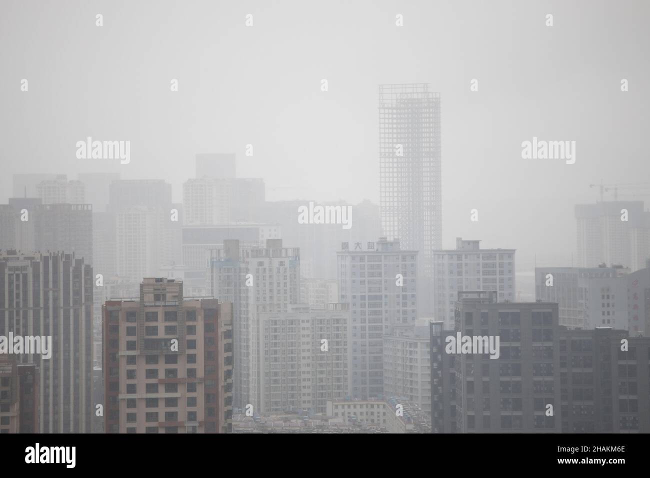 Neblige, rauchige, deprimierende chinesische Stadt mit vielen Gebäuden und KRÄNEN Stockfoto