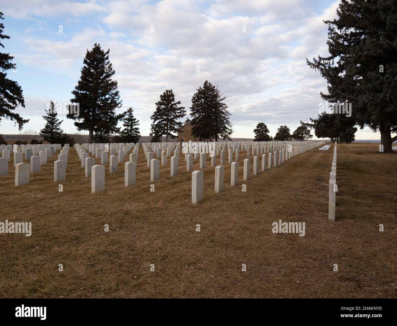 Reihen von Grabsteinen aus weißem Marmor auf dem Custer National Cemetery im Little Bighorn Battlefield National Monument in Montana. Das ursprüngliche Parkgebäude Stockfoto