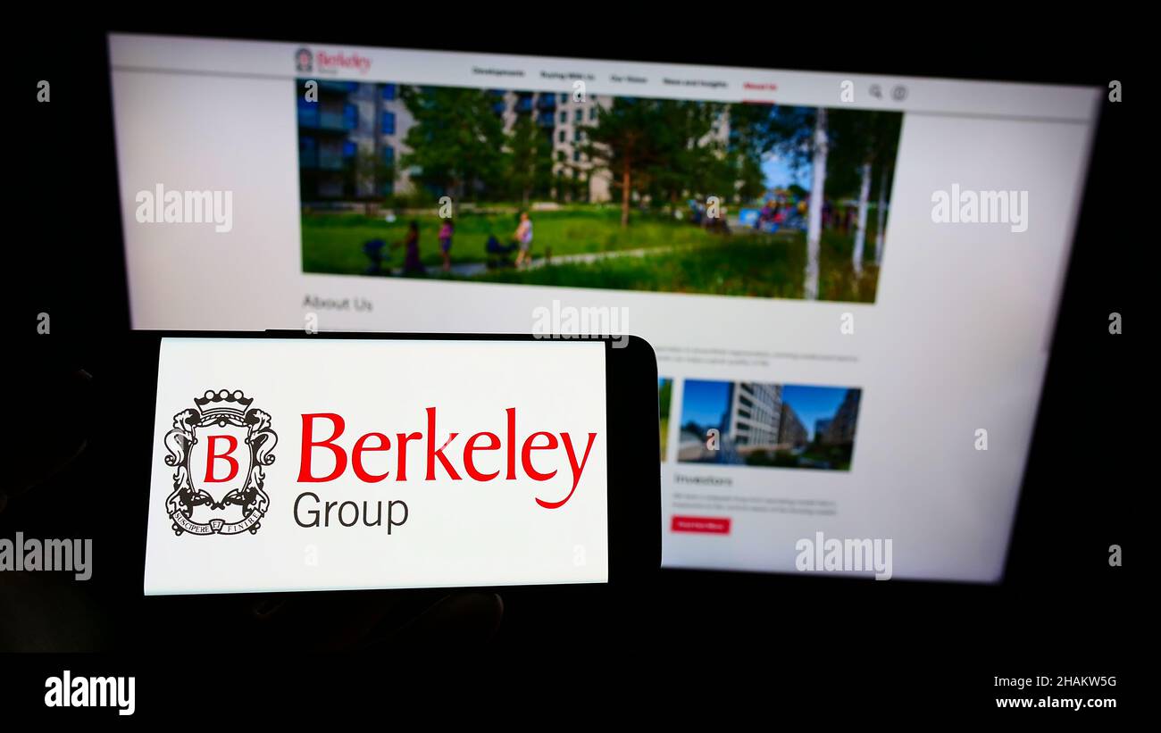 Person mit Mobiltelefon und Logo des britischen Unternehmens The Berkeley Group Holdings plc auf dem Bildschirm vor der Webseite. Konzentrieren Sie sich auf die Telefonanzeige. Stockfoto