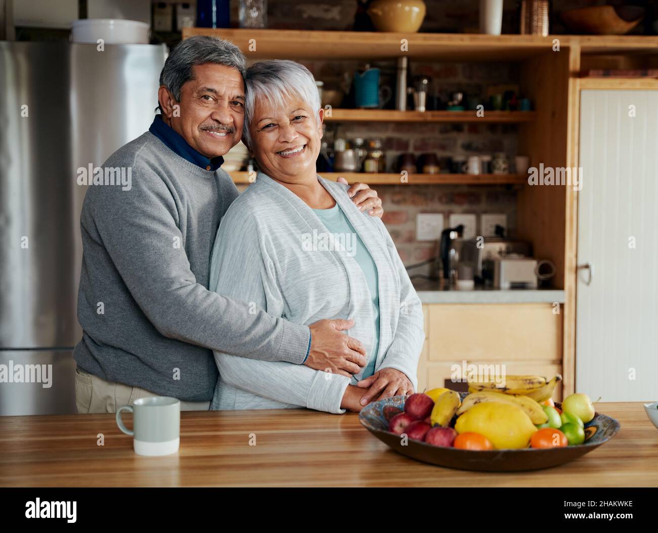 Porträt eines glücklich pensionierten älteren Birazialpaares, das in der Küche steht, umarmt und lächelt. Stockfoto