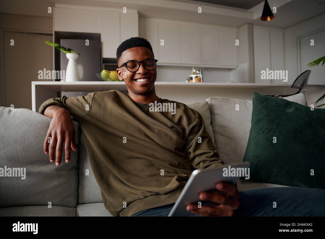 Junger, erwachsener schwarzer Mann, der auf dem Tablet lächelt, während er auf dem Sofa sitzt Stockfoto
