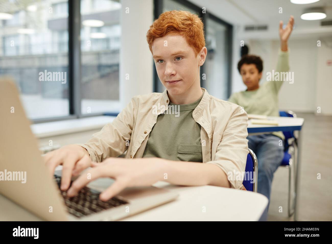 Porträt eines rothaarigen Jungen im Teenageralter, der einen Laptop in einem Codierungskurs für Kinder benutzt, Kopierraum Stockfoto