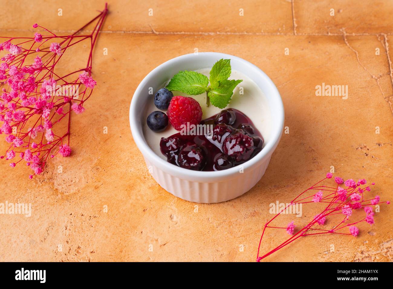 Schicke Panna Cotta mit Beeren-Marmelade und Minze auf braunem Hintergrund rosa Blüten Stockfoto