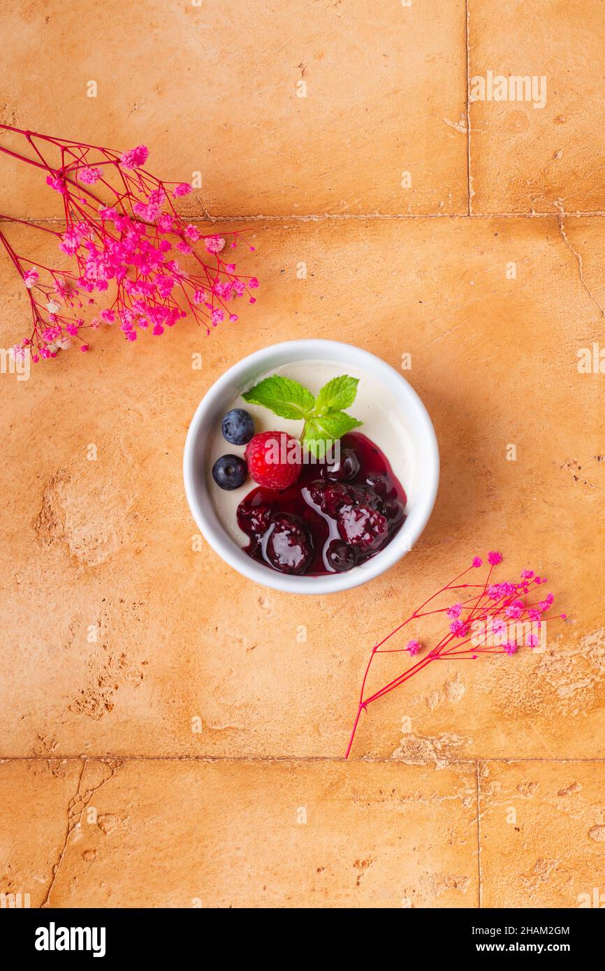 Schicke Panna Cotta mit Beeren-Marmelade und Minze auf braunem Hintergrund rosa Blüten Stockfoto