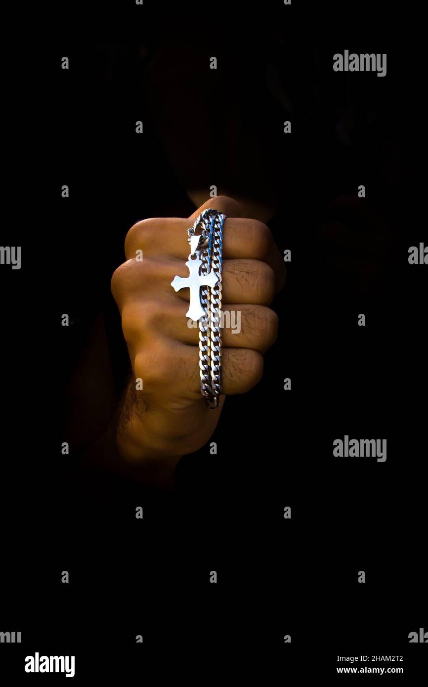 Hand hält eine silberne Halskette mit Kreuzanhänger auf schwarzem Hintergrund Stockfoto