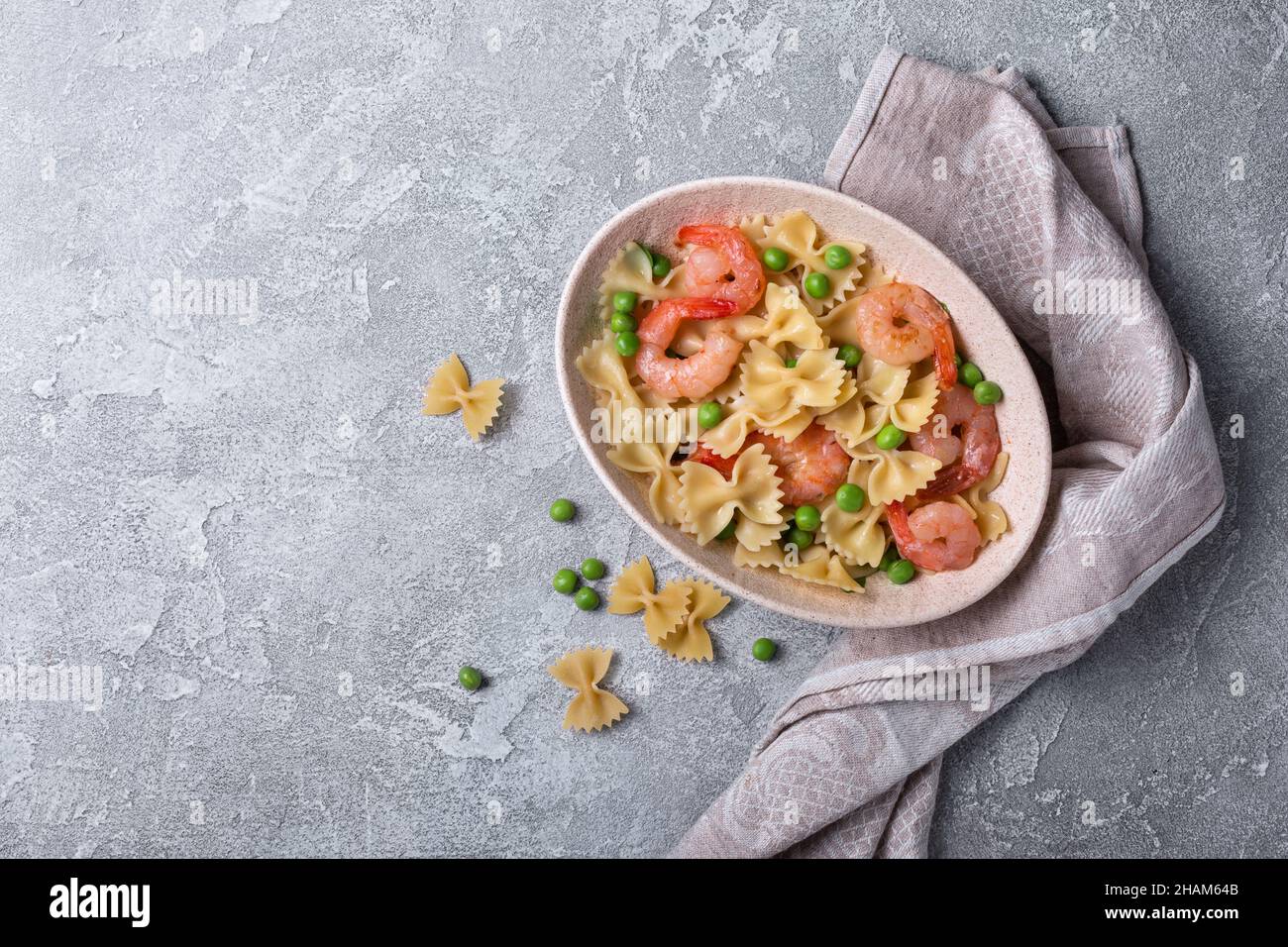 Draufsicht auf leckere italienische Farfalle-Pasta mit Garnelen oder Garnelen und grünen Erbsen auf grauem Beton-Hintergrund Stockfoto