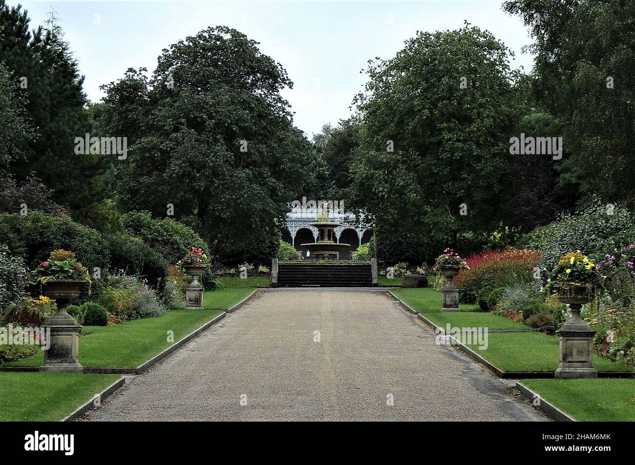 OLDHAM, VEREINIGTES KÖNIGREICH - 14. Sep 2016: Ein Park Gehweg, der von Rasen und Blumenbeeten und großen Bäumen gesäumt ist, in der Ferne Stufen und Bandstand in Oldham Stockfoto