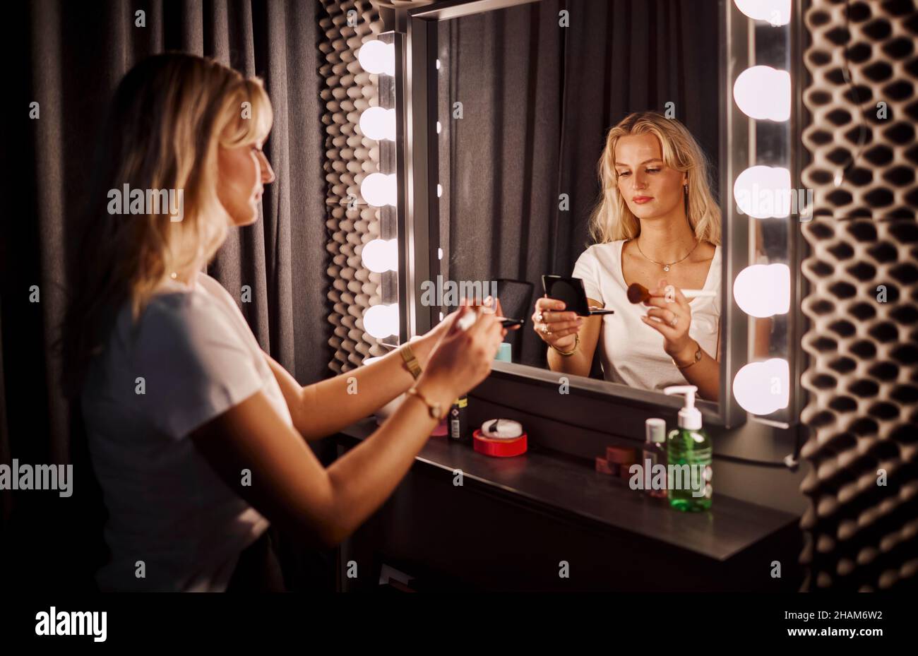 Junge Frau, die Make-up vor dem Spiegel aufführt Stockfoto