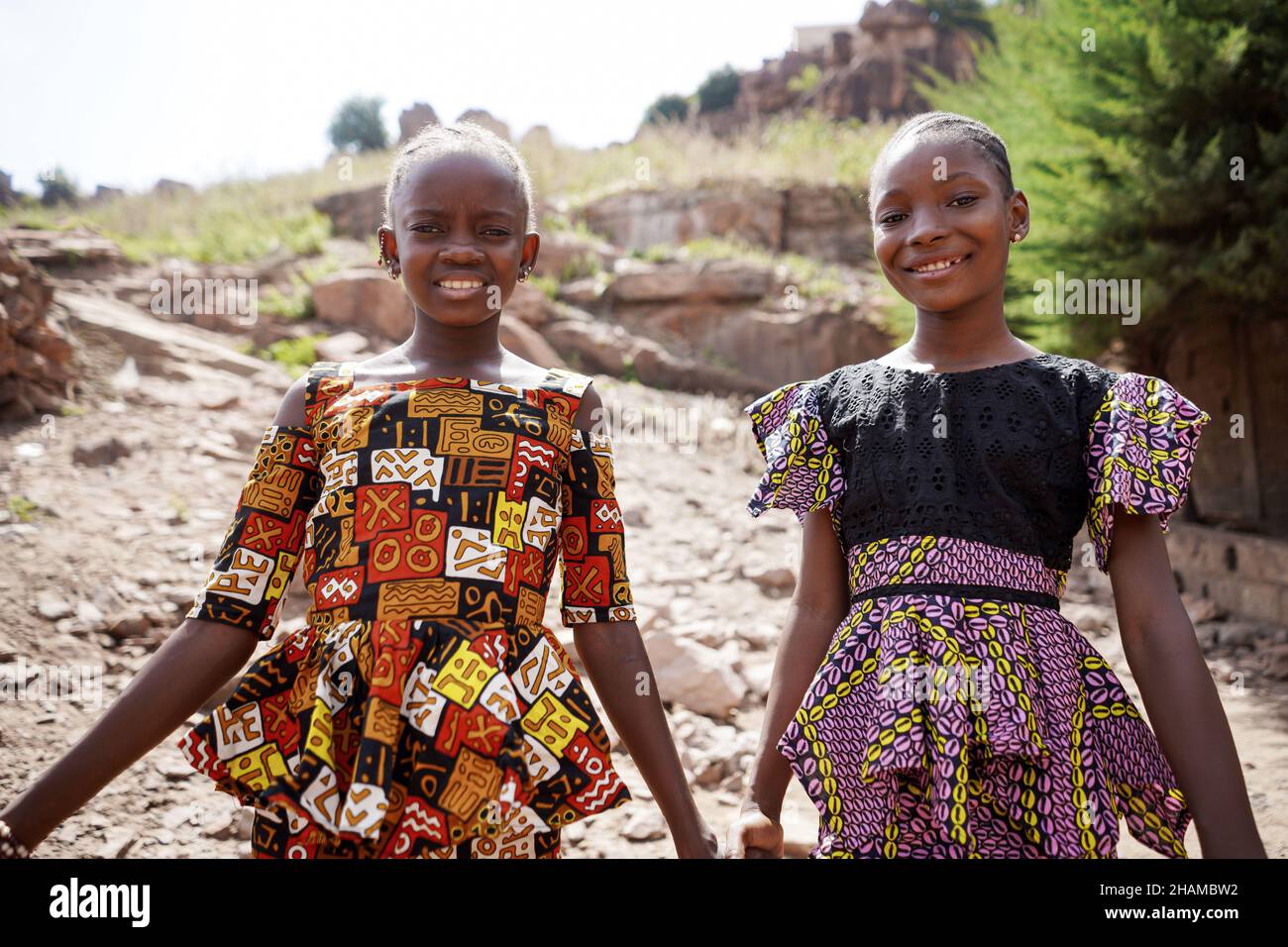 Zwei glückliche Mädchen stehen mit Smiley-Gesichtern in der Natur mit traditionellem neuen afrikanischen Kleid zusammen Stockfoto