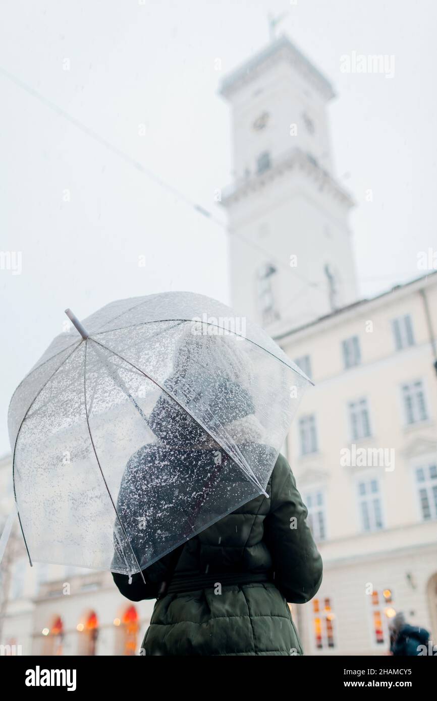 Frau, die im Stadtzentrum von Lviv am Rathaus mit Regenschirm unter Schnee herumläuft. Tourist genießt Architektur im Winter. Reisen in der Ukraine Stockfoto