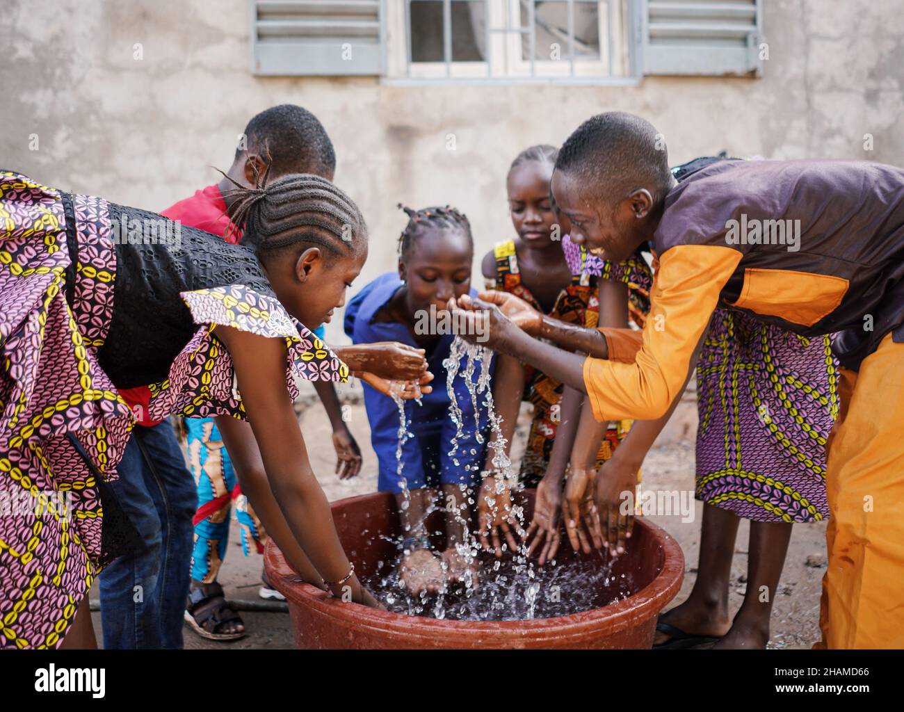 Eine große Gruppe junger afrikanischer Kinder spielt in einem armen Dorf in Mali mit Wasser aus dem Eimer Stockfoto