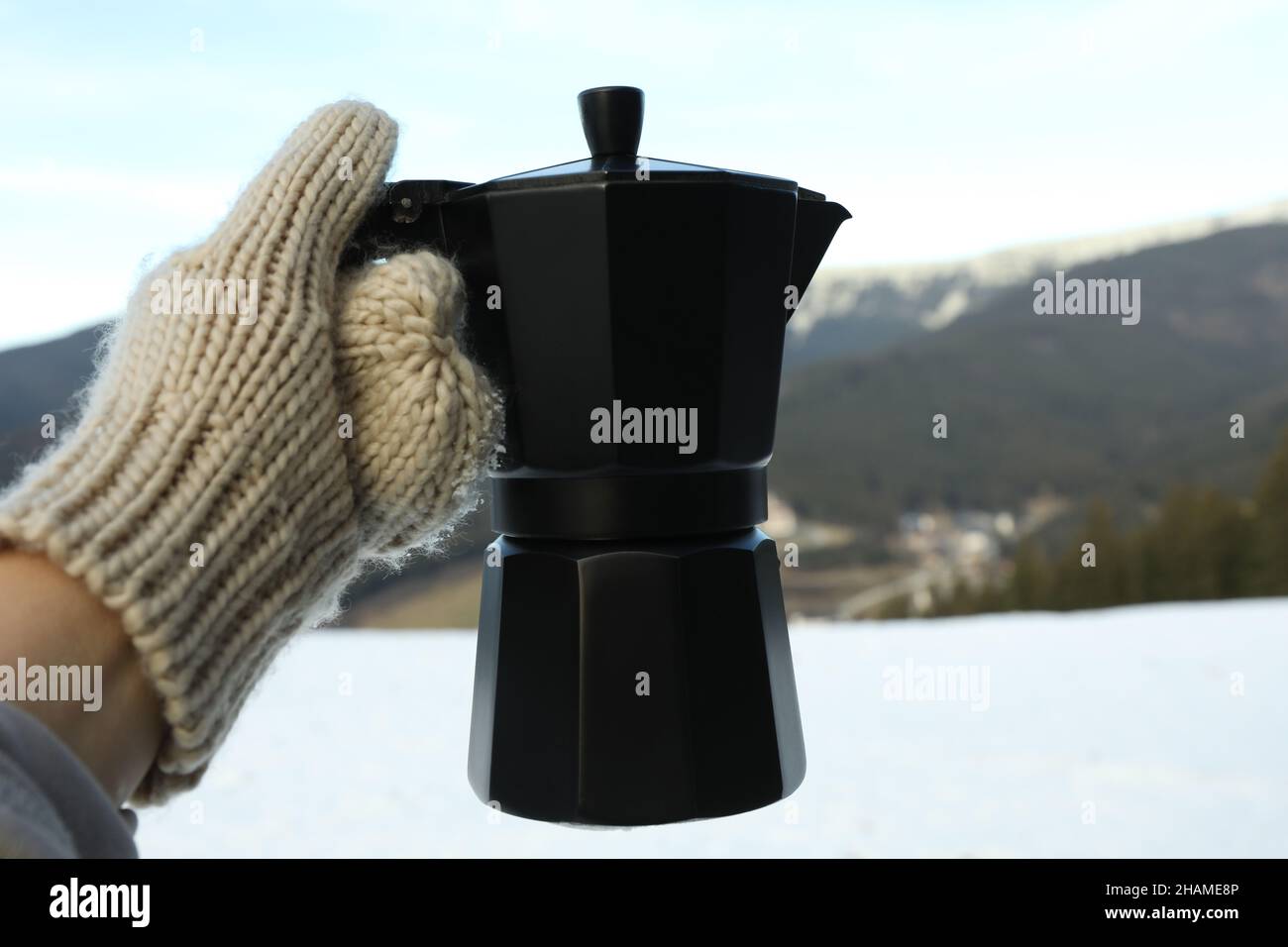 Hand in Fäustling hält die Kaffeemaschine gegen die Berge Stockfoto